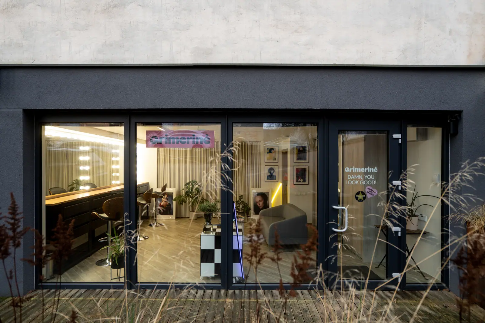Grimerinė beauty studio storefront in Vilnius: glass frontage and open door, salon name on the window, the slogan on the door, and the makeup and lounge area visible inside.